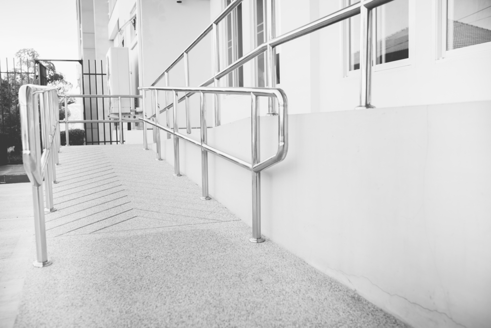 A grayscale image of a modern, outdoor concrete ramp with metal railings on both sides, providing accessibility to a building.