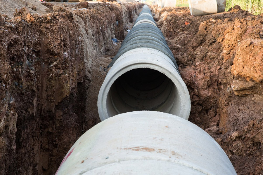 Close-up of a large concrete pipe being laid in a trench with exposed earth, part of underground infrastructure or construction work.